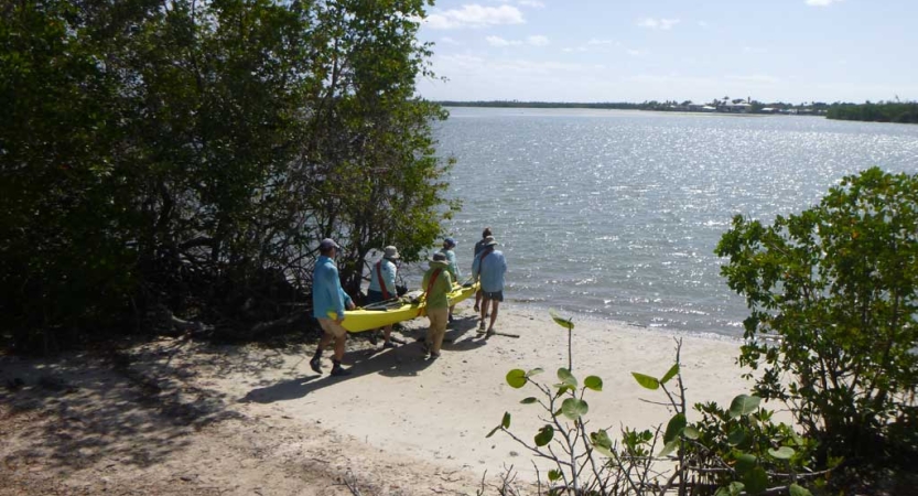 A group of people carry a kayak into the water from a sandy beach